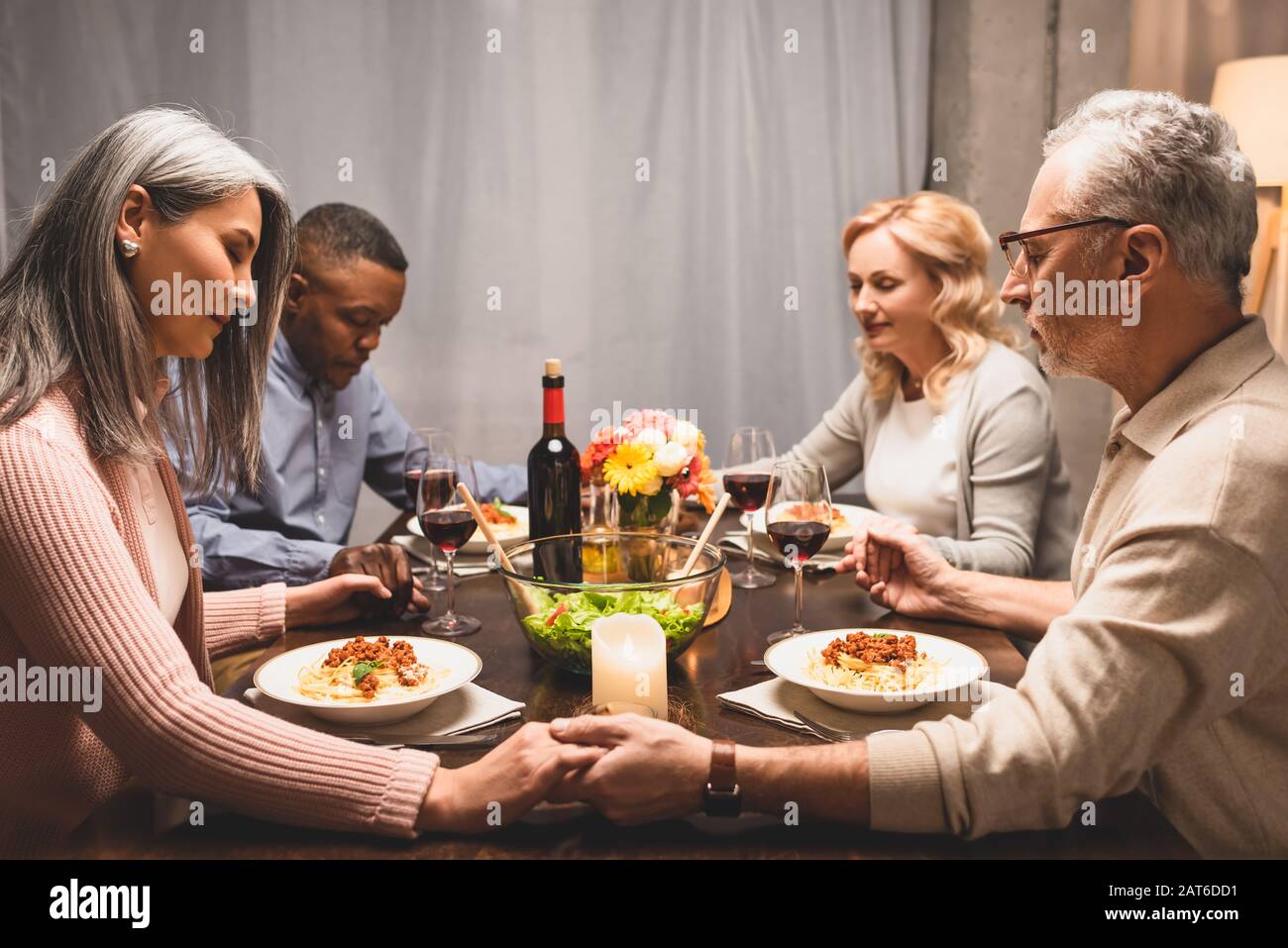 multicultural friends holding hands and praying during dinner Stock