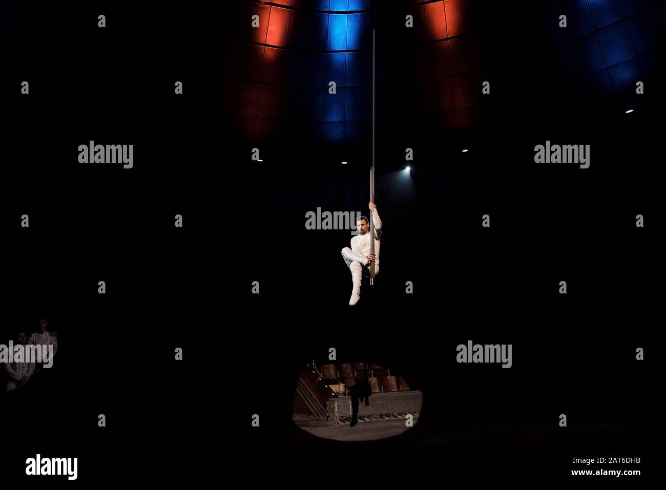 spotlights on acrobat performing acrobatic exercise on metallic pole in circus Stock Photo