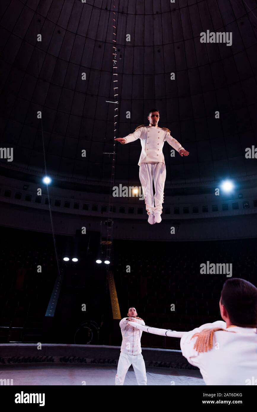 acrobats holding pole while handsome man jumping in circus Stock Photo