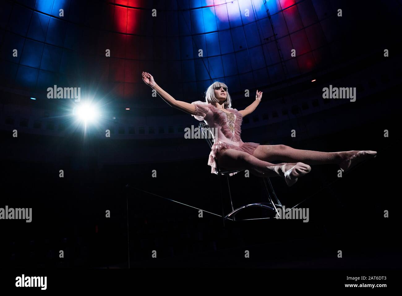 aerial acrobat with outstretched hands balancing on rope while sitting ...