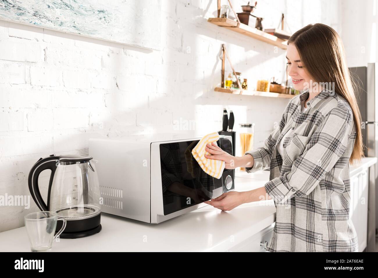 smiling and attractive woman cleaning microwave with rag in kitchen Stock Photo