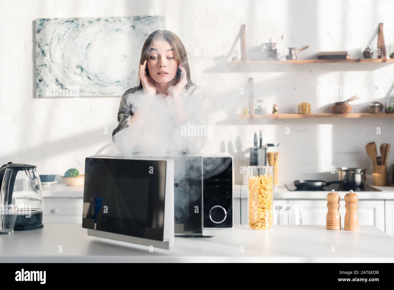 shocked and attractive woman looking at broken microwave in kitchen
