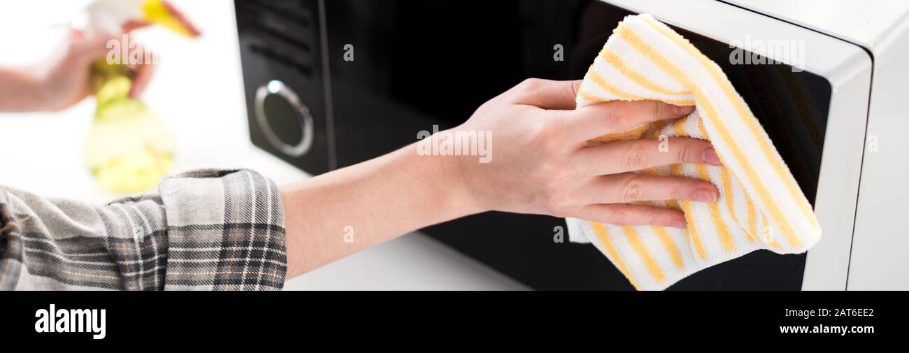 panoramic shot of woman cleaning microwave with rag in kitchen Stock Photo