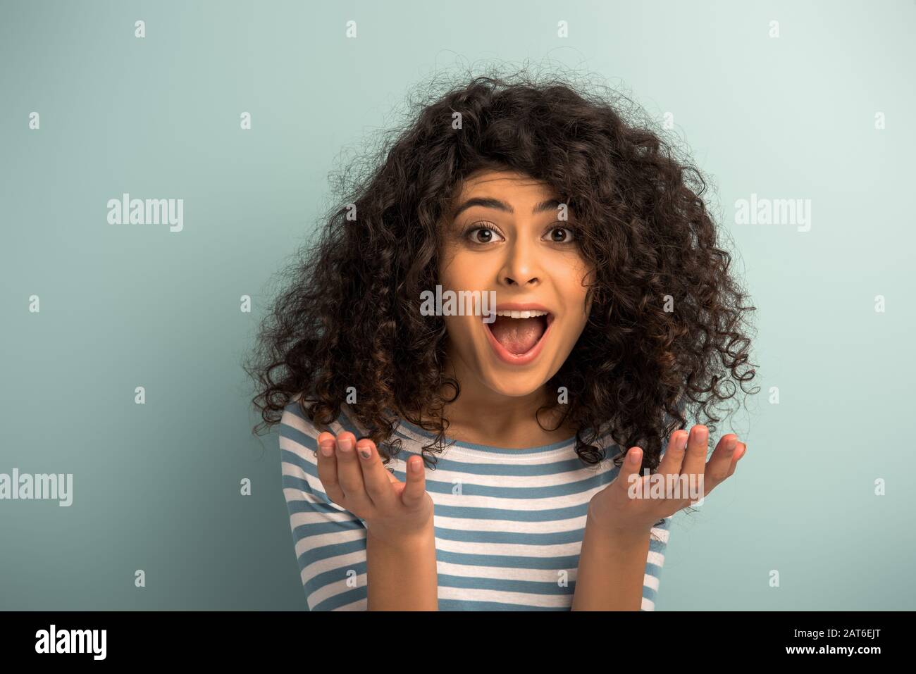 irritated mixed race girl shouting at camera and showing indignation gesture on grey background Stock Photo