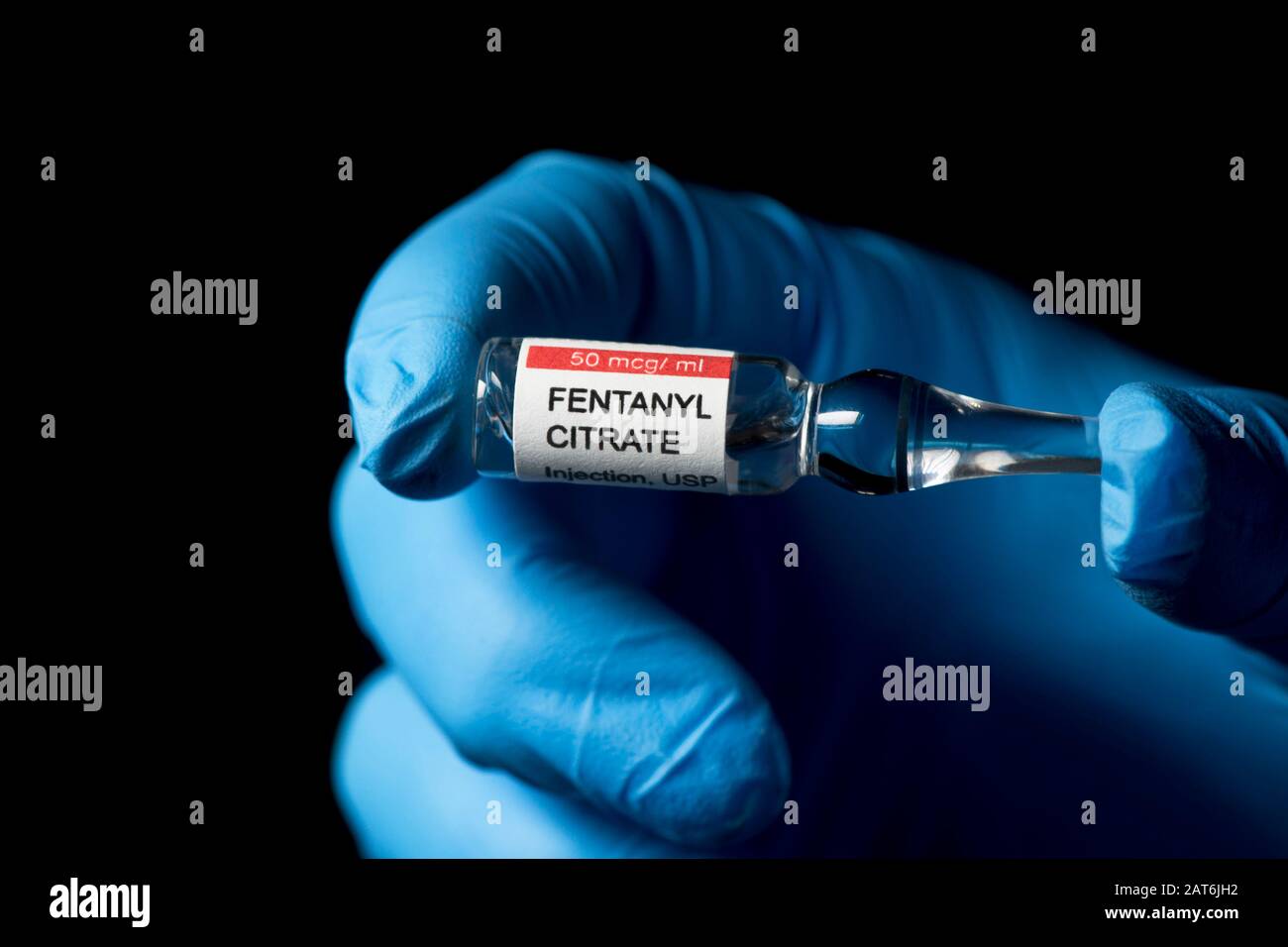 Fentanyl citrate injection ampule held by gloved hand of healthcare worker with dark background. Stock Photo