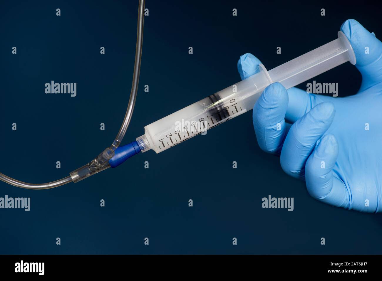 Nurse flushes IV medication port with sodium chloride solution syringe on dark background. Stock Photo