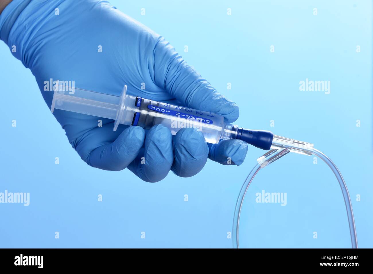 Nurse flushes IV medication port with heparin solution syringe on blue background. Stock Photo