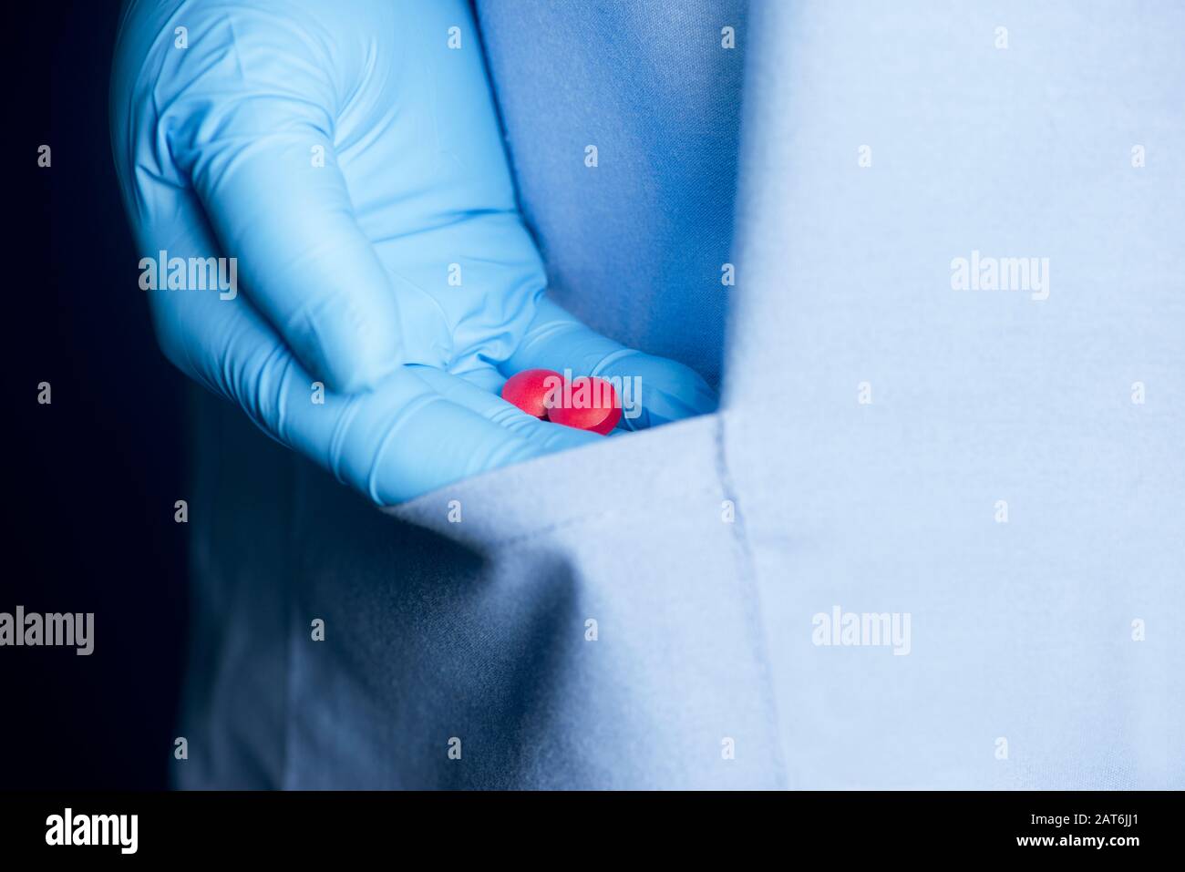 Gloved hand of healthcare worker slips narcotic medication tablets  into pocket of scrub shirt. Stock Photo