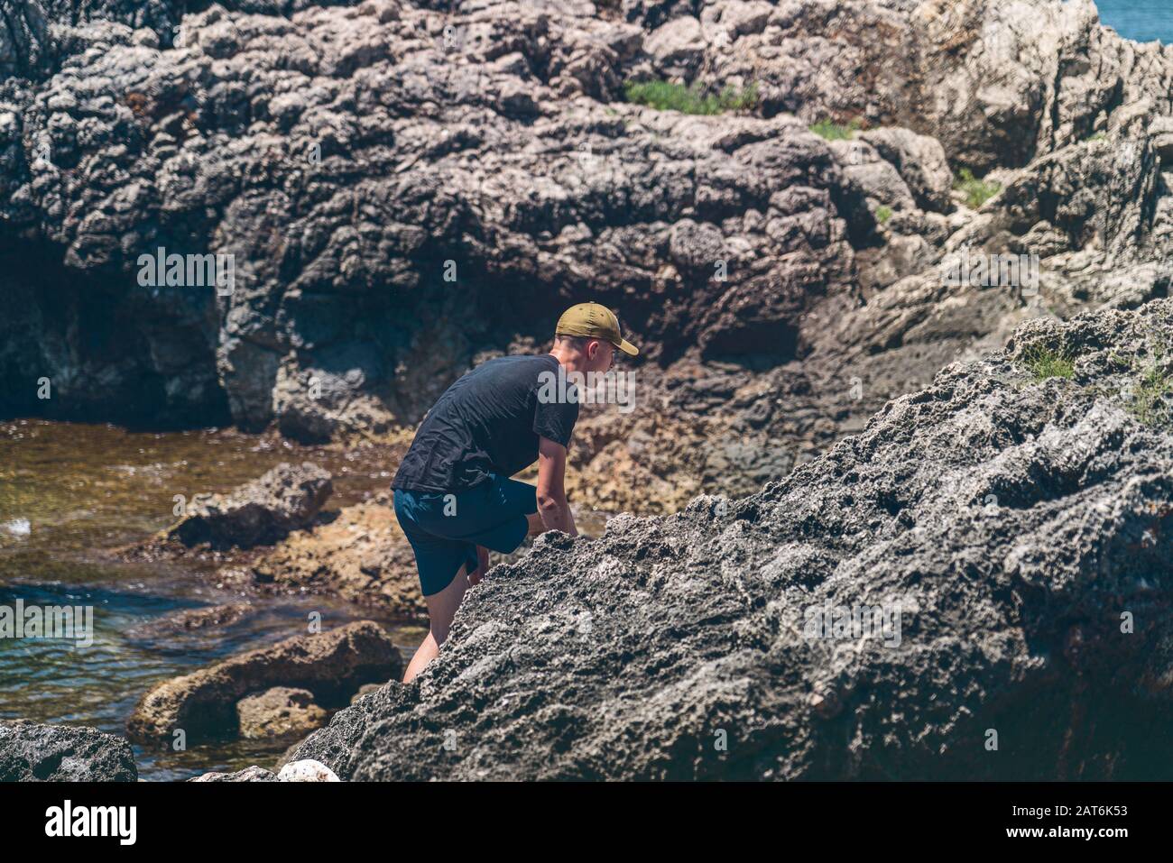 https://c8.alamy.com/comp/2AT6K53/young-man-with-baseball-cap-climbs-through-the-sharp-rocks-by-the-sea-2AT6K53.jpg