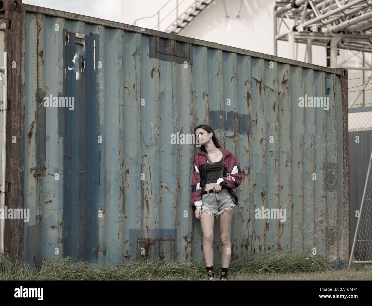 Modern teenager girl standing by old well used grungy looking cargo container desaturated for old faded effect. Stock Photo