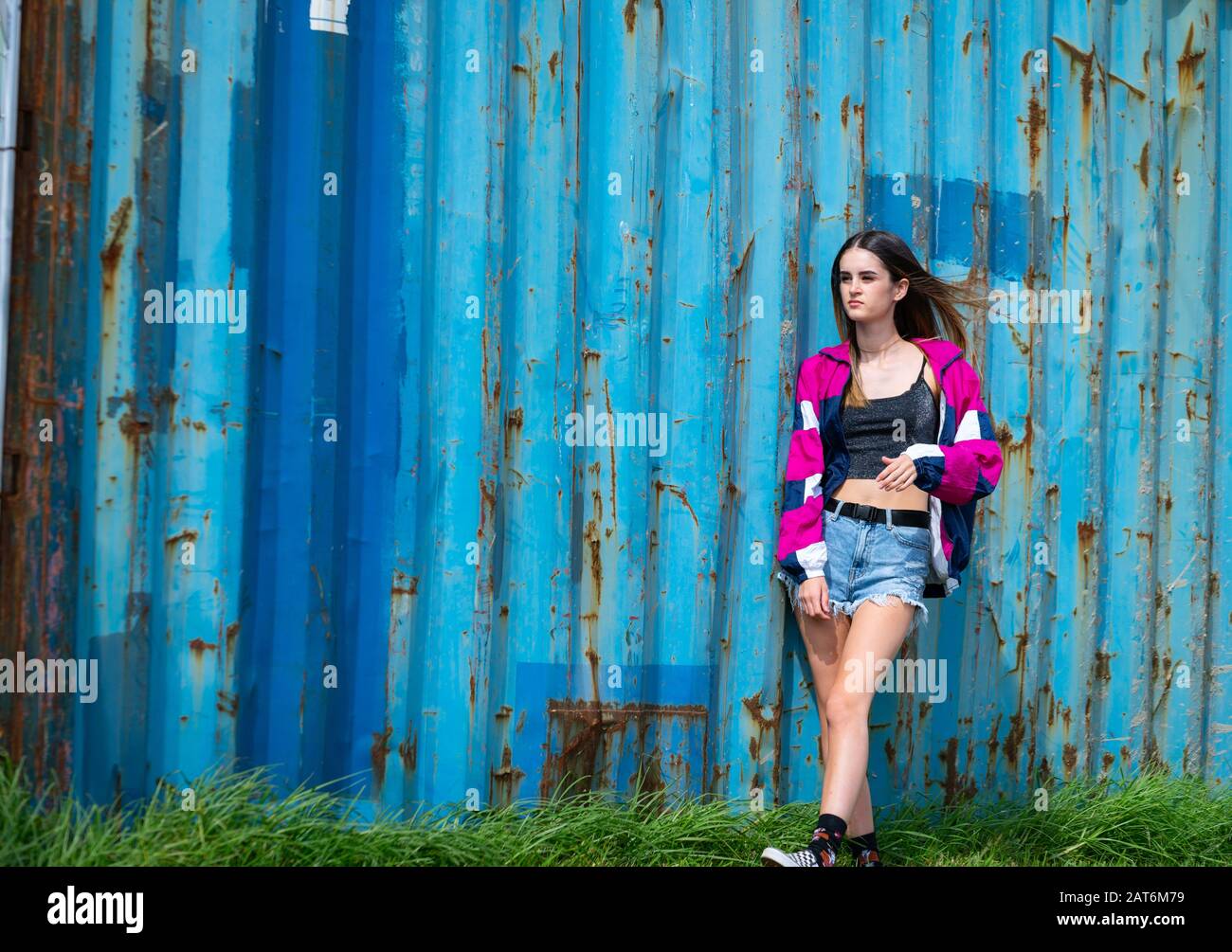 Modern teenager girl standing by old well used grungy looking cargo container, Stock Photo