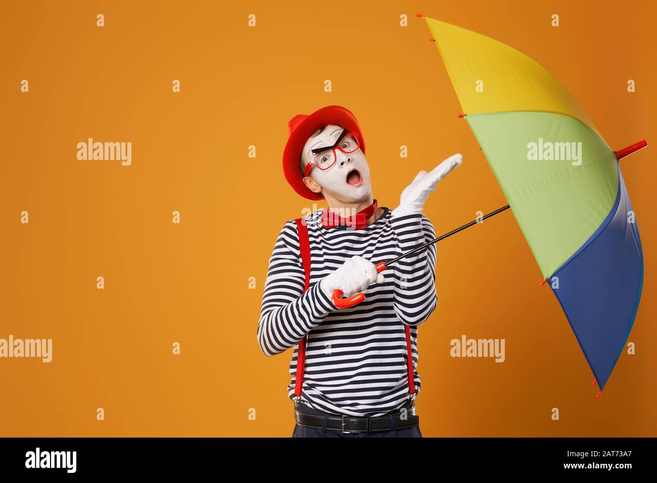 One mime with multi-colored umbrella on empty orange background in studio Stock Photo