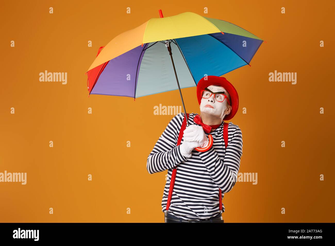 Mime with multi-colored umbrella on empty orange background in studio Stock Photo