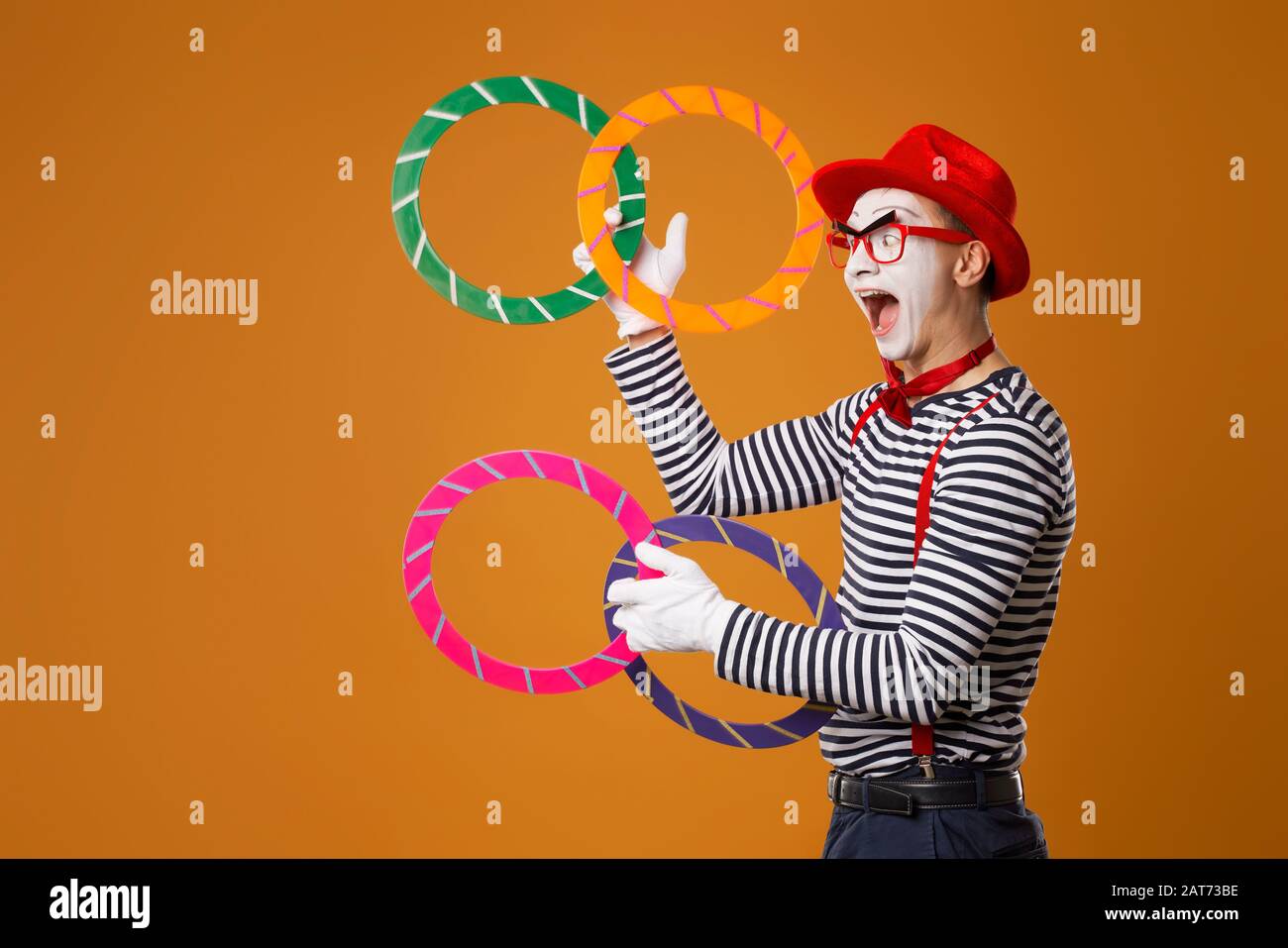 Happy mime with multi-colored rings on empty orange background Stock Photo