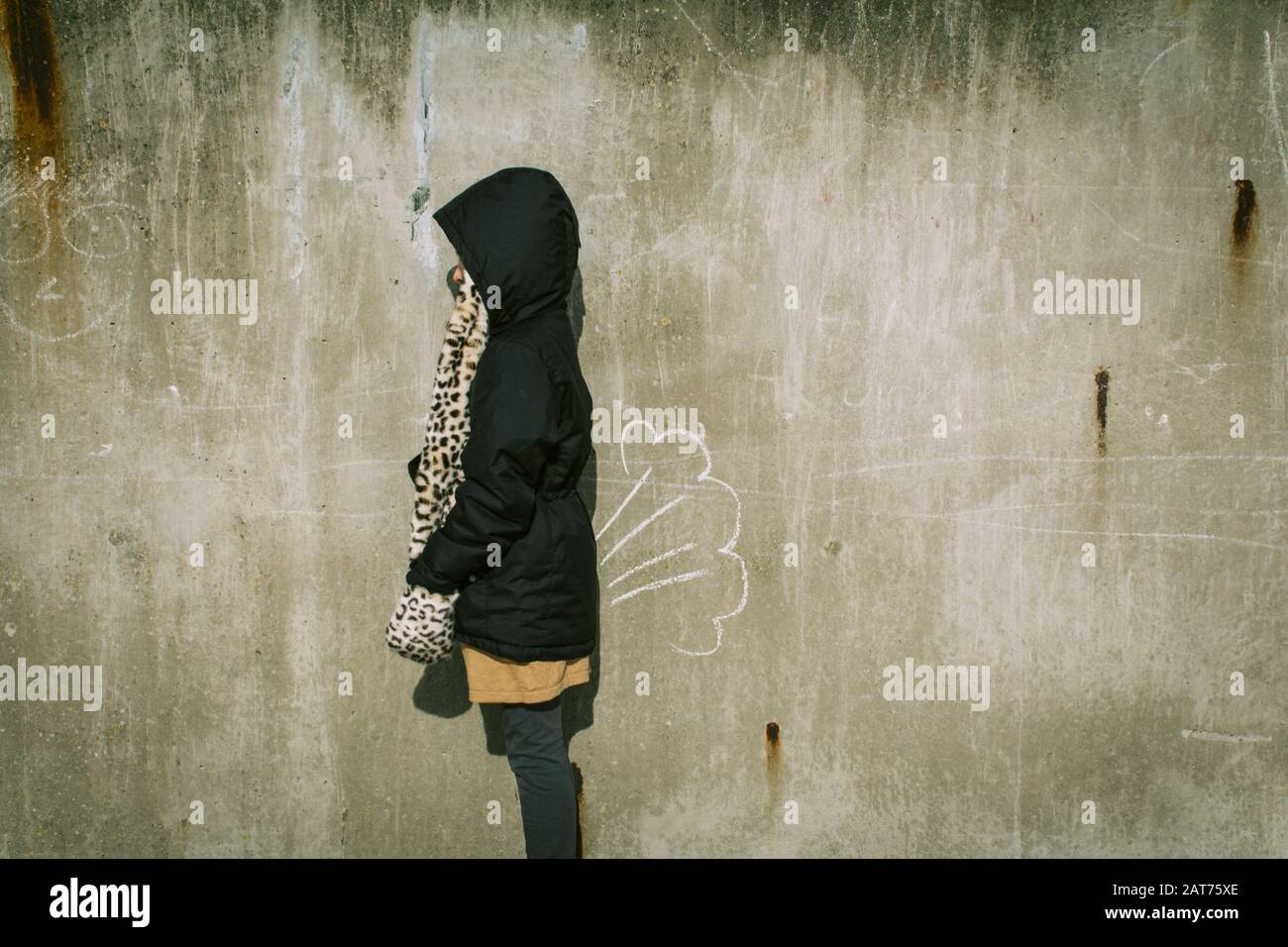 Person with a black coat standing in front of an old painted wall Stock Photo