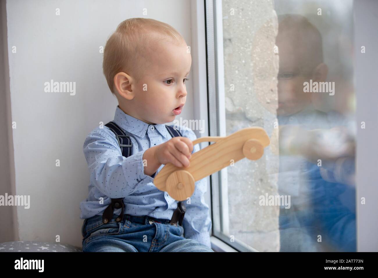 Kid Window Toy A small child looks out the window. The kid with a toy sits on a window ...