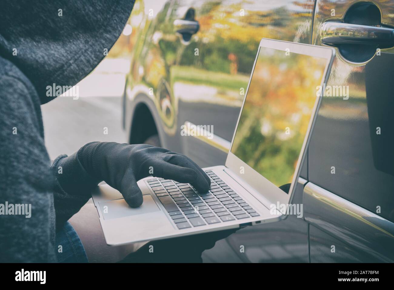 Hooded thief tries to break the car's security systems with laptop