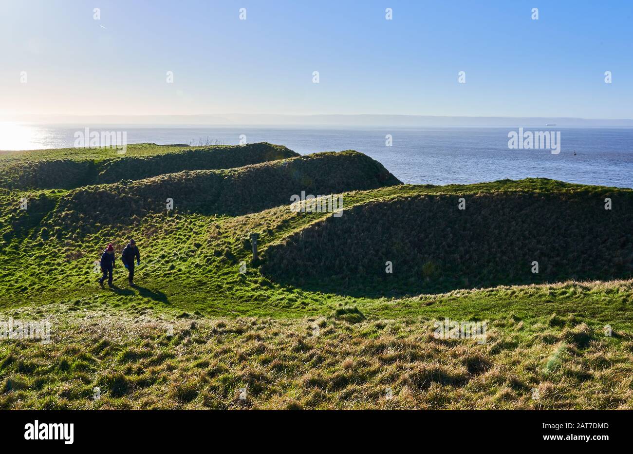 Walkers on the Wales Coast Path passing the earthworks of Nash Point Iron Age Hill Fort on the Glamorgan coast of South Wales Stock Photo