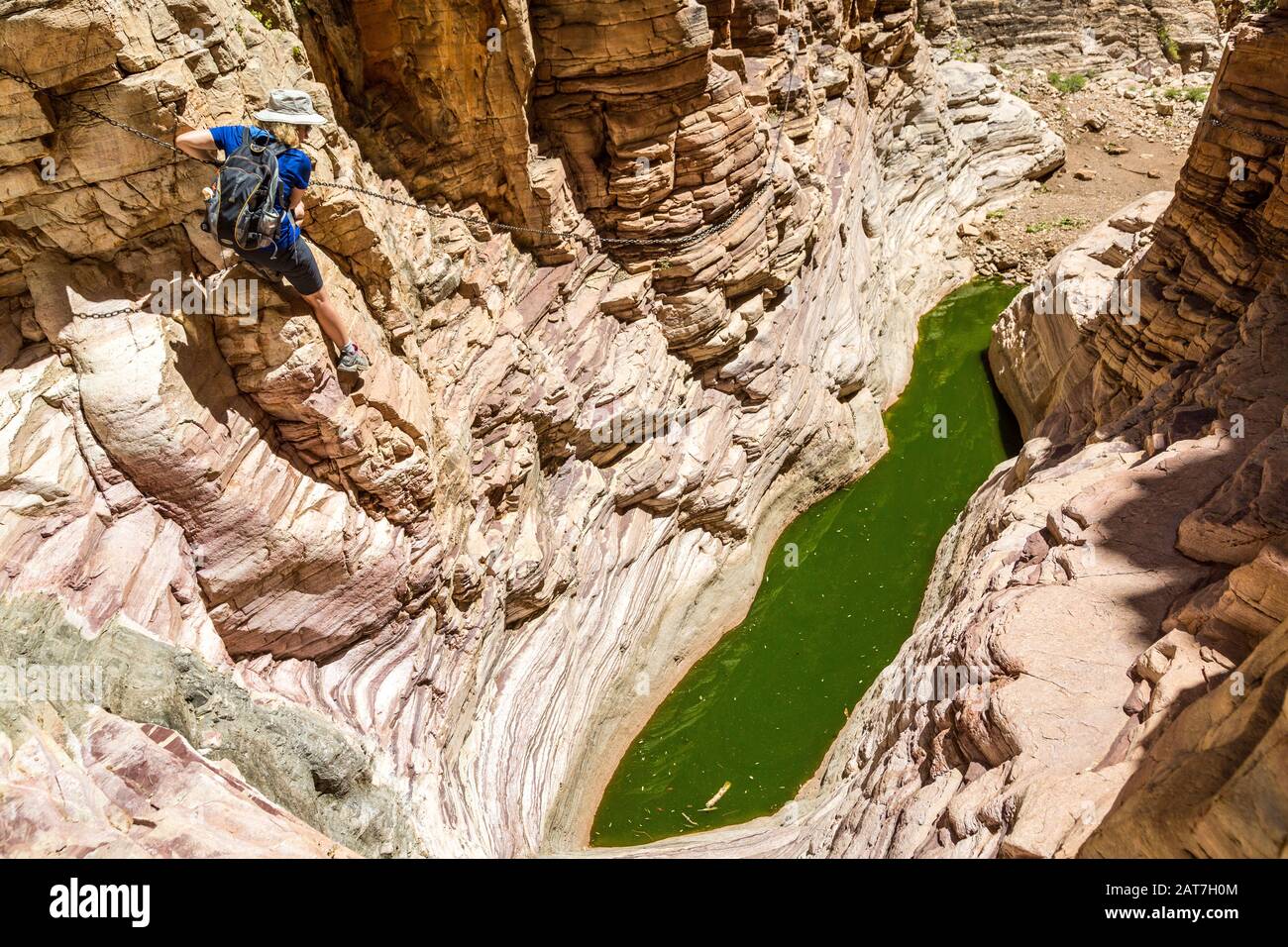Young woman climbing down in a canyon with a natural pool at the bottom and steep rock faces around it, Olive Trail, Namib Naukluft Park, Namibia Stock Photo