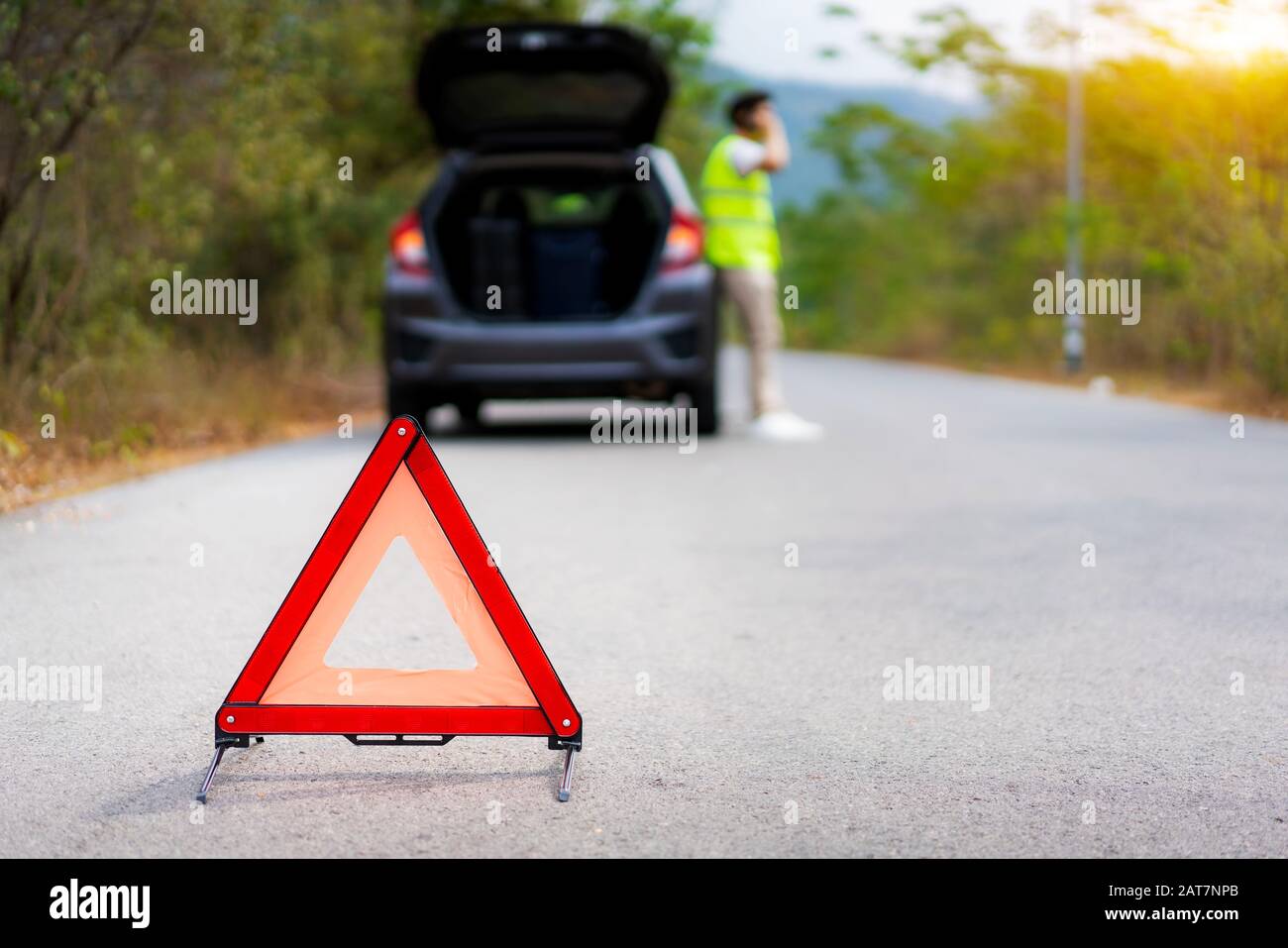 Breakdown triangle sign on road with worried Asian man talking by mobile phone with insurance or car service center company after car breakdown on cou Stock Photo