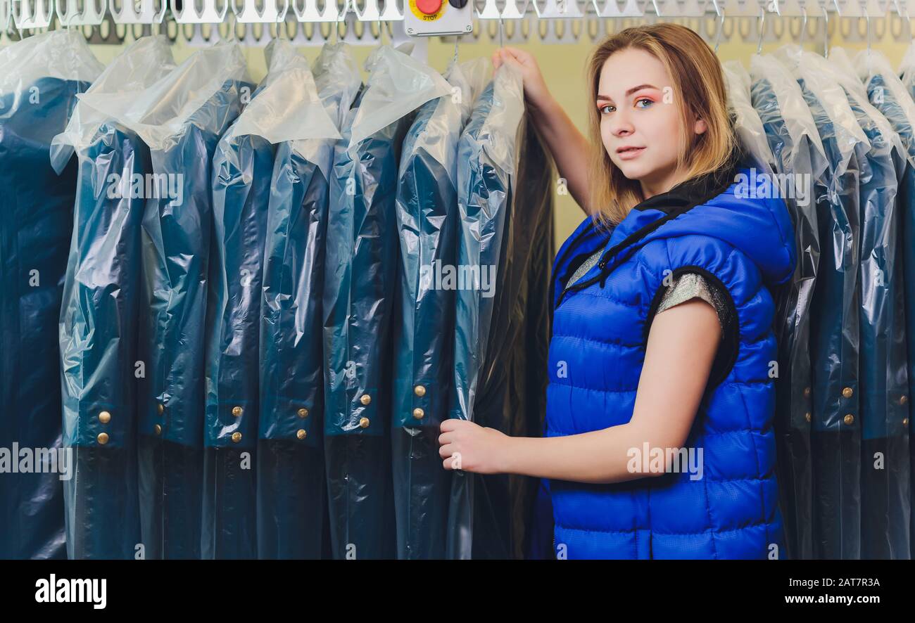 Female cleaner in laundry shop or textile drycleaning next to clean clothes in garment bags