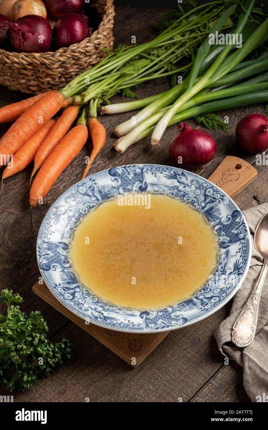 Chicken bone broth in a vintage plate, with fresh vegetables in the