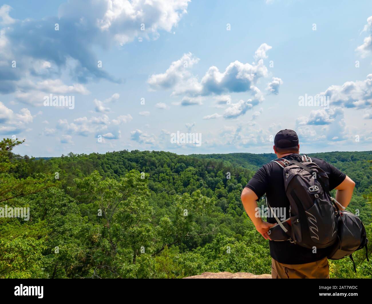 Man, hiker, standing on top of the Natural Bridge in Kentucky looking out into the sky filled with clouds from way up high, over the tree tree tops. Stock Photo