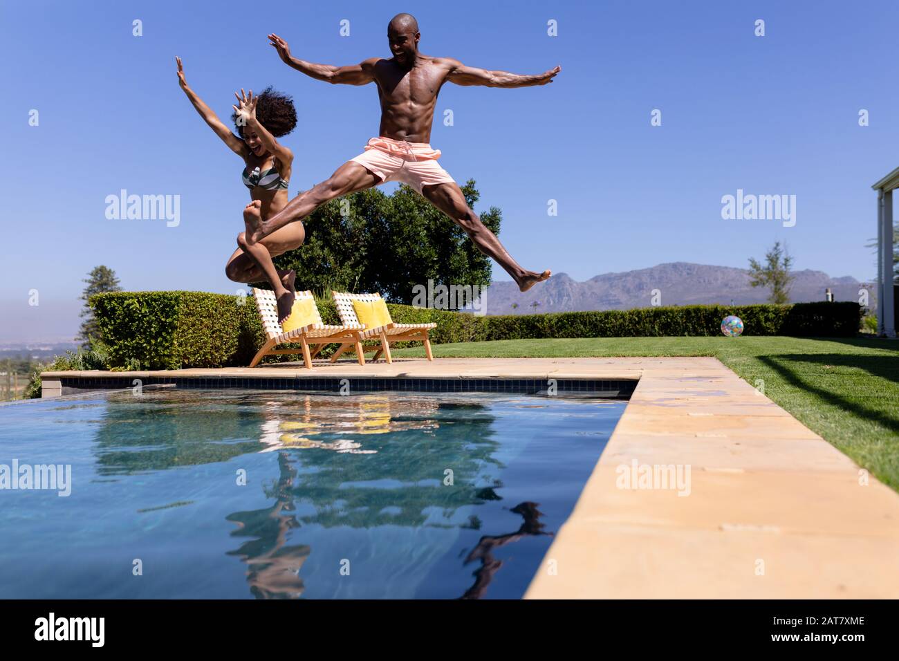 Young couple jumping on swimming pool on a sunny day Stock Photo