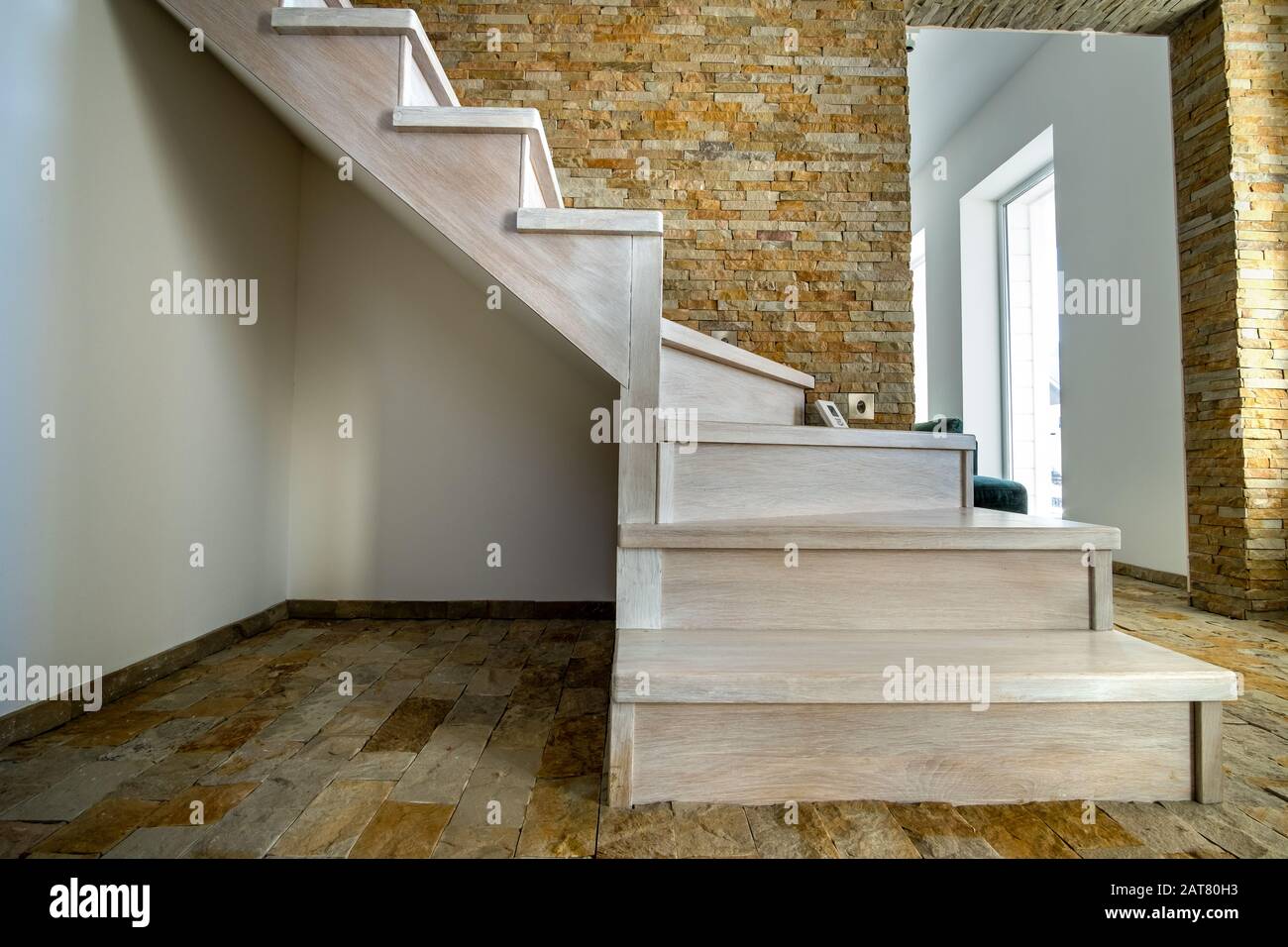 Stylish wooden contemporary staircase inside loft house interior. Modern hallway with decorative limestone brick walls and white oak stairs. Stock Photo