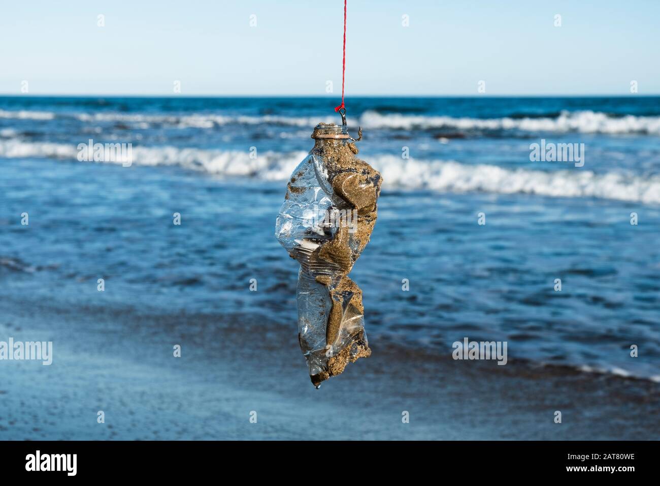 closeup of a used plastic bottle, covered with wet sand, in a fish hook, freshly fished in the ocean Stock Photo