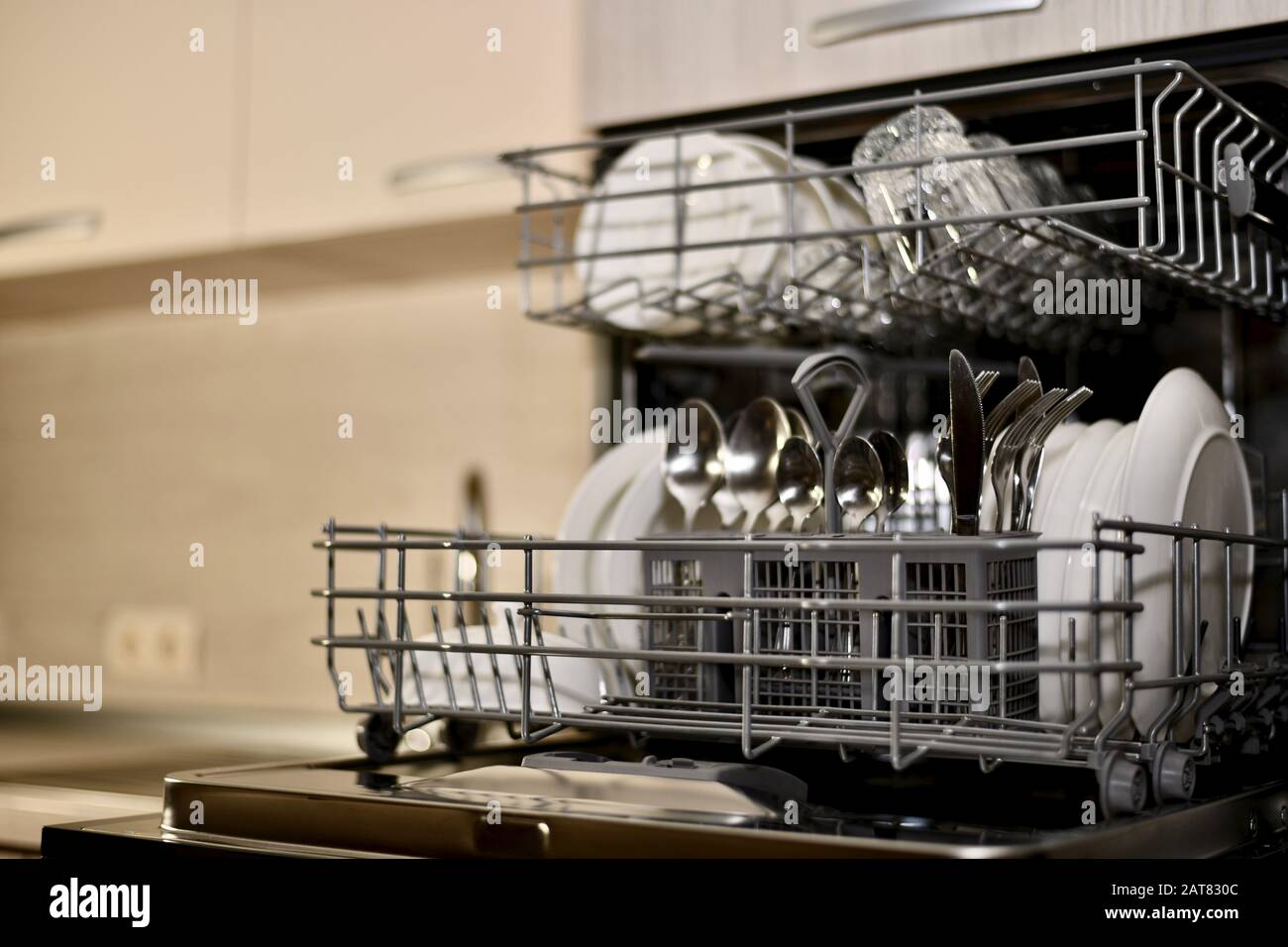 A dishwasher with dishes built in the kitchen cabinet opened an angle view with a perspective and almost complete blur. Stock Photo