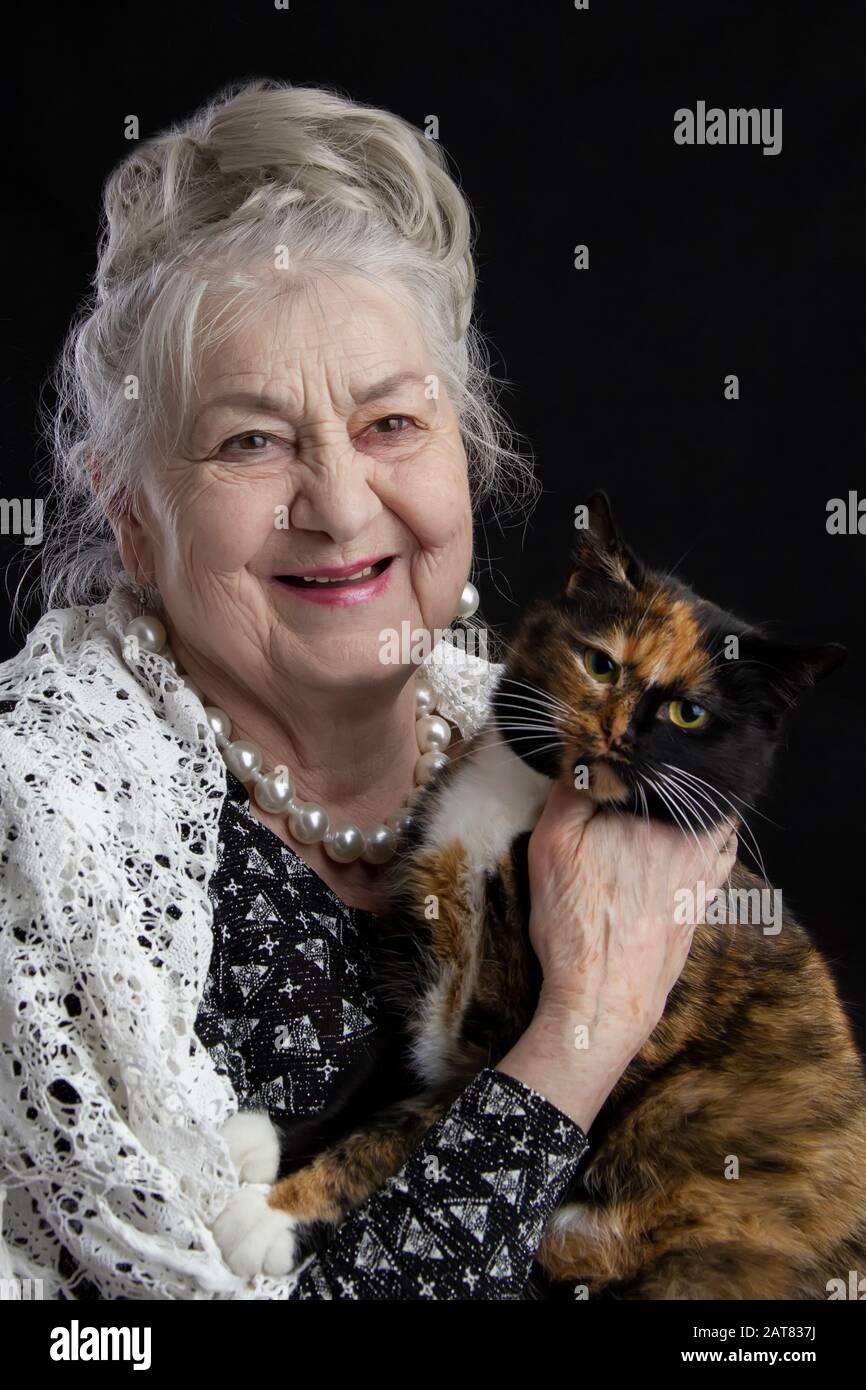 Portrait of a ninety year old woman with a pet. Merry old lady with a cat. Grandmother on a black background with a furry animal. Elderly beauty. The Stock Photo