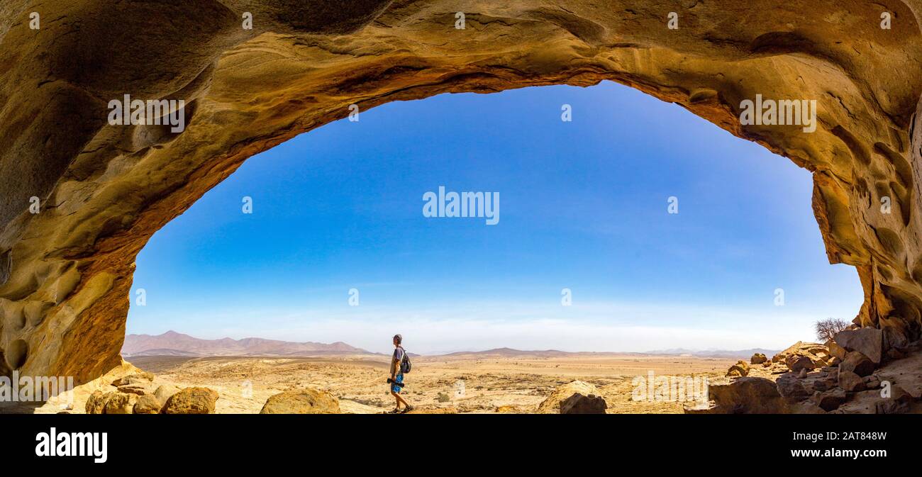 Panoramic view from a cave at Blutkuppe over the desert of Namib Naukluft Park, a man walking under the rock dome, Namibia, Africa Stock Photo