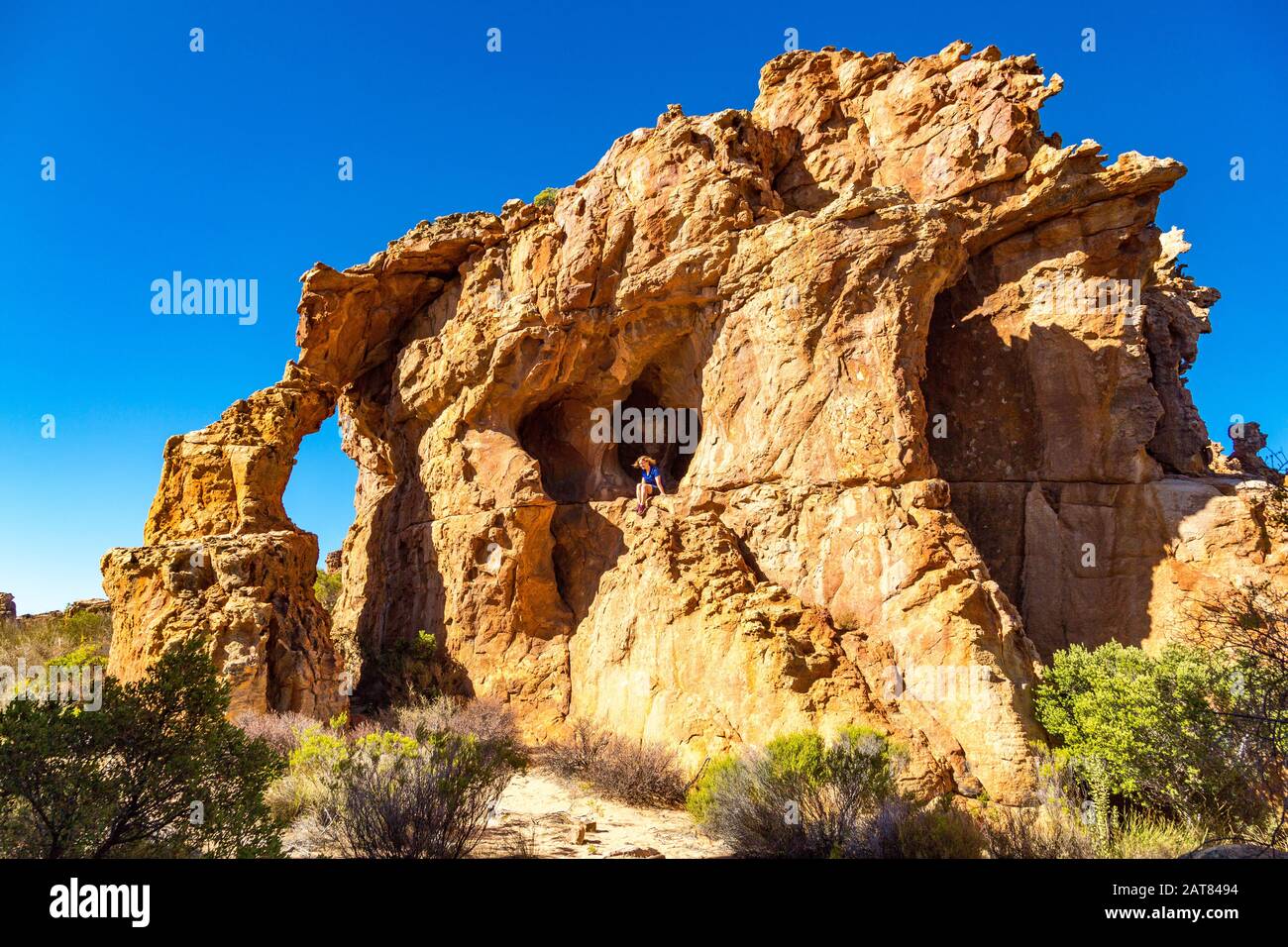 Spectacular rock formation with arch and cave, young woman sitting on an exposed rock, Stadsaal, Cederberg Wilderness Area, South Africa Stock Photo