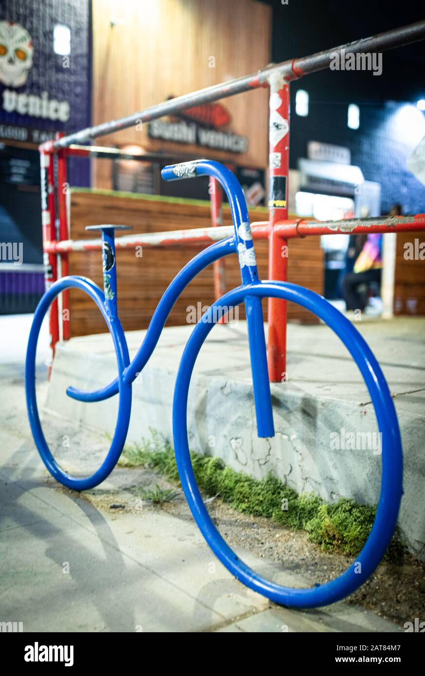 A modern art installation in Venice, California featuring a colorful bike in front of a fence and stores. Stock Photo