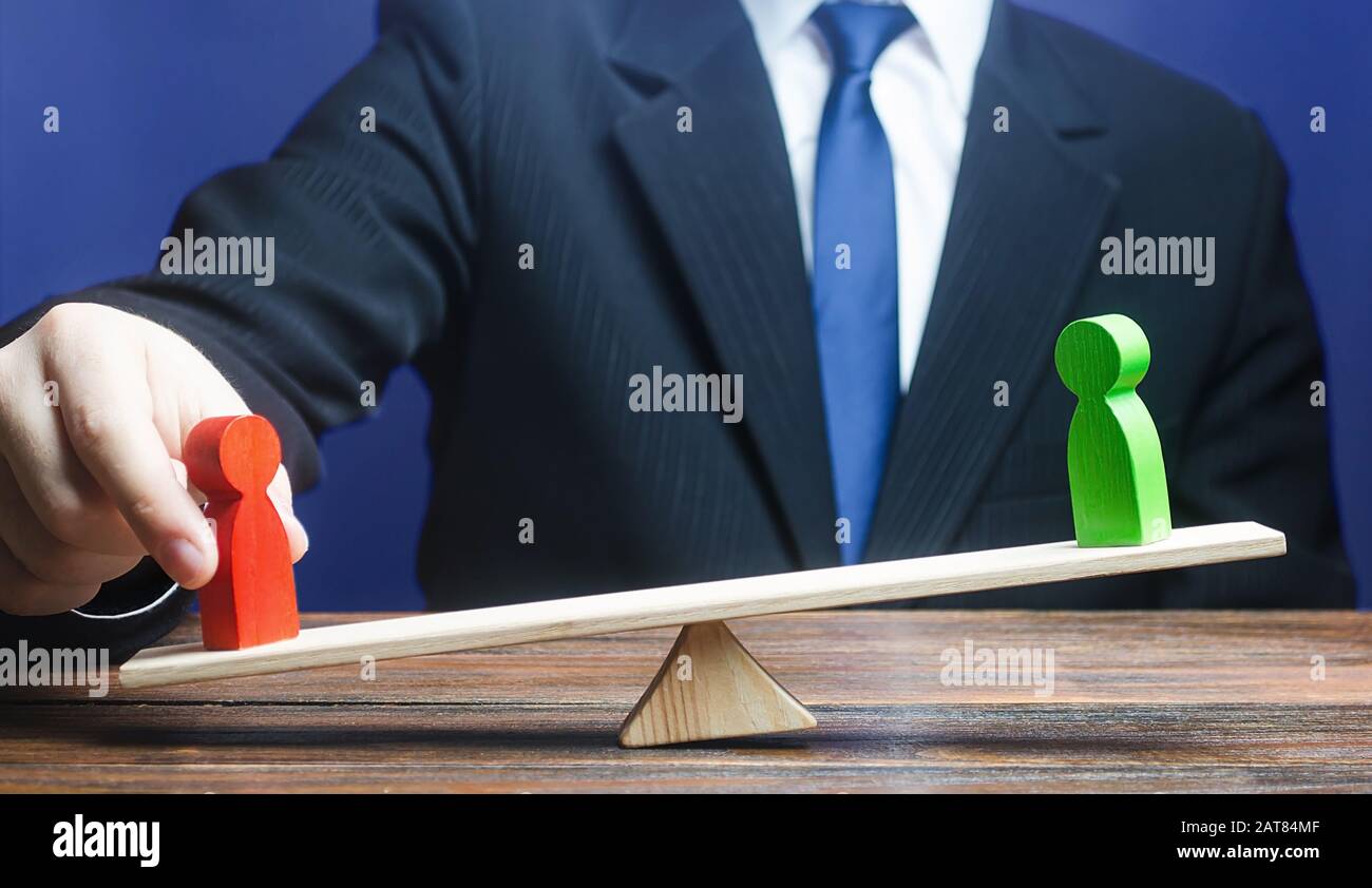 Man opposes green figure to red opponent on scales. Give an advantage, change balance of power, change outcome of confrontation. Invisible helping han Stock Photo