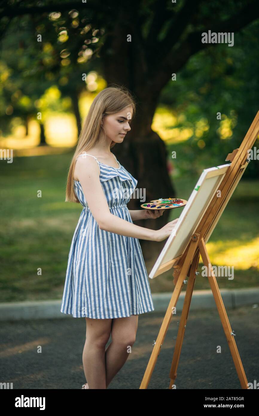 Beautiful girl draws a picture in the park using a palette with paints ...