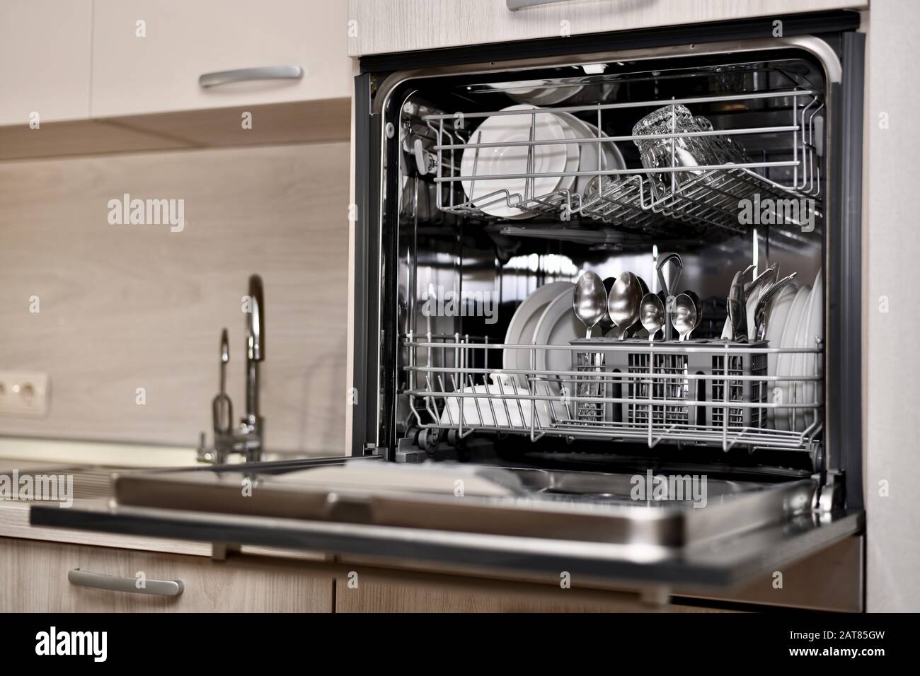 A dishwasher with utensils opened, installed at the sink level with a dryer and two taps