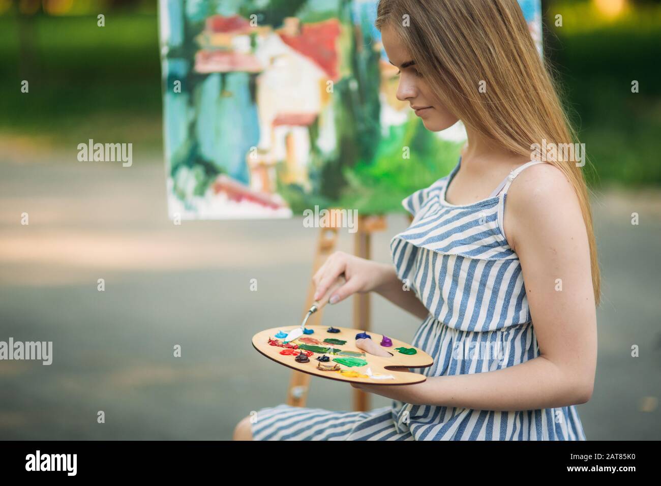 Beautiful girl draws a picture in the park using a palette with paints ...