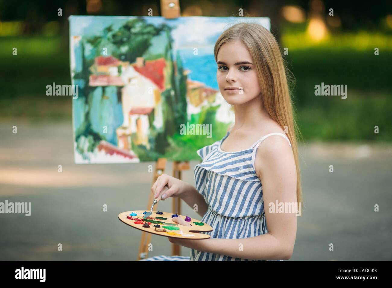 Beautiful girl draws a picture in the park using a palette with paints ...