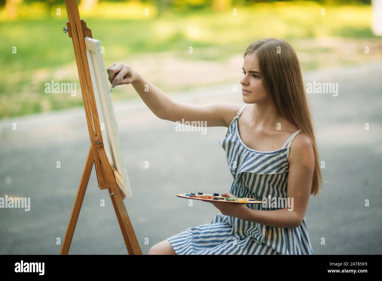 Beautiful girl draws a picture in the park using a palette with paints ...