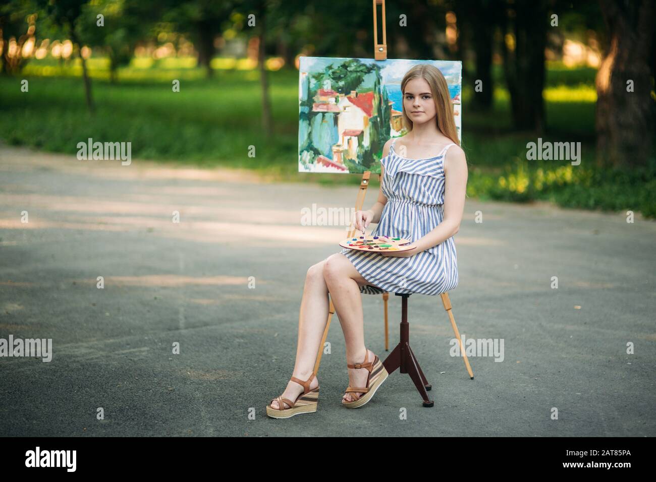 Beautiful girl draws a picture in the park using a palette with paints ...