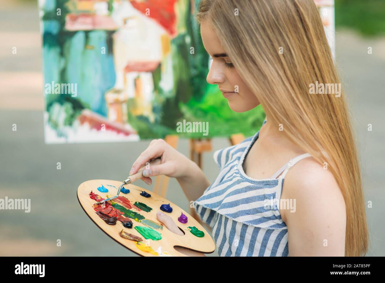 Beautiful girl draws a picture in the park using a palette with paints ...