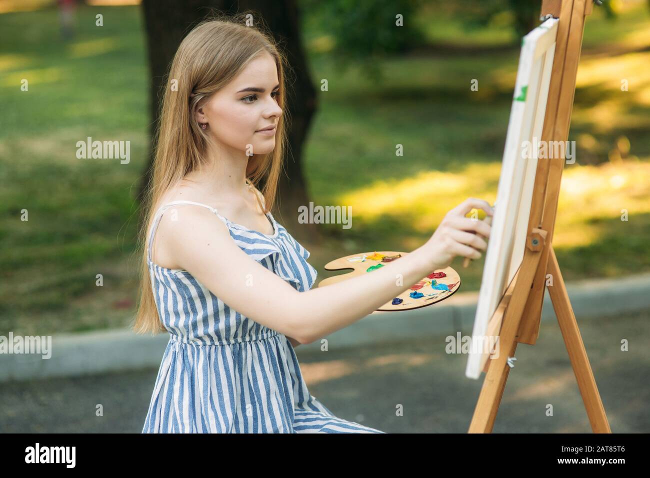 Beautiful girl draws a picture in the park using a palette with paints ...