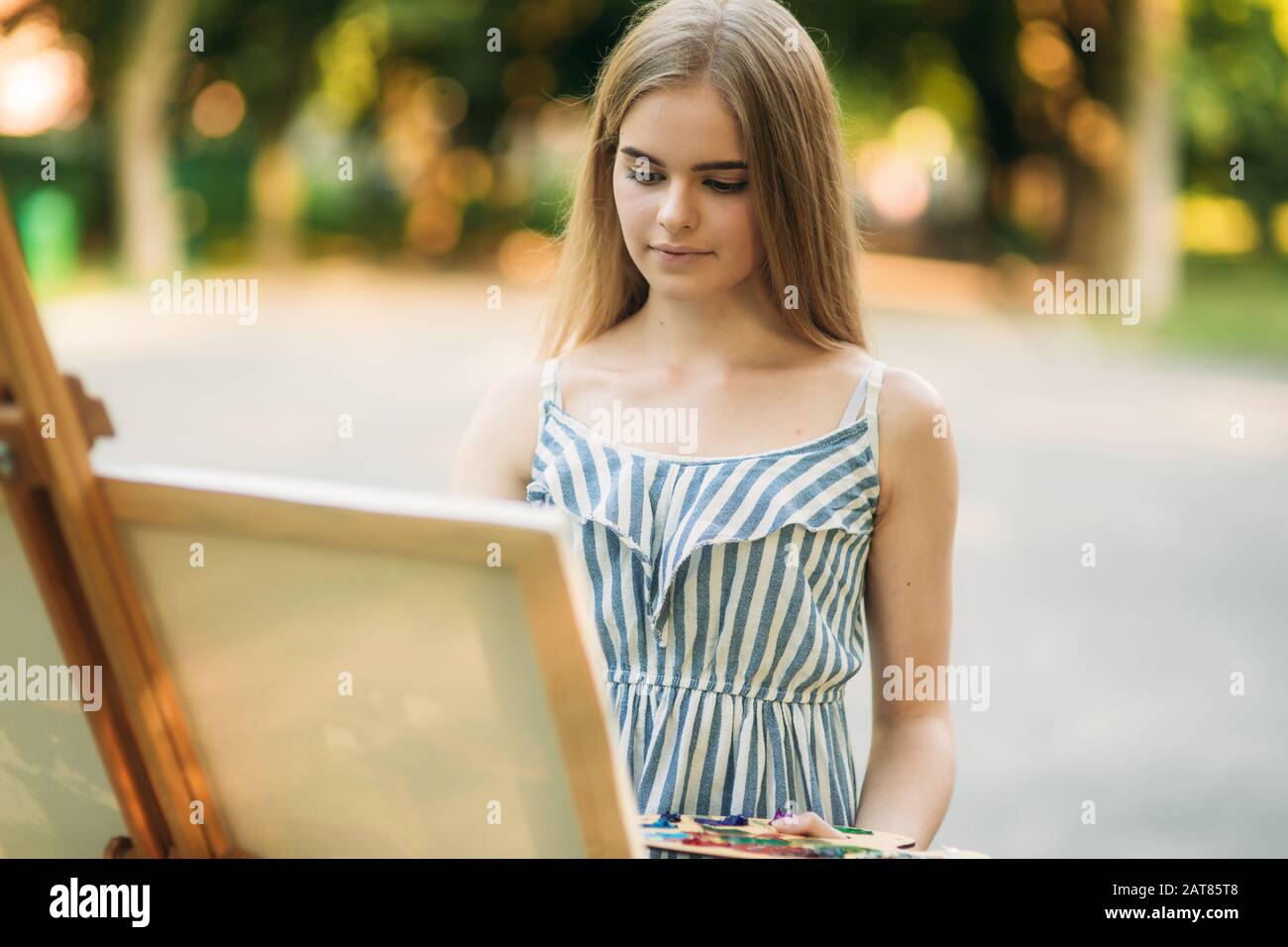 Beautiful girl draws a picture in the park using a palette with paints ...