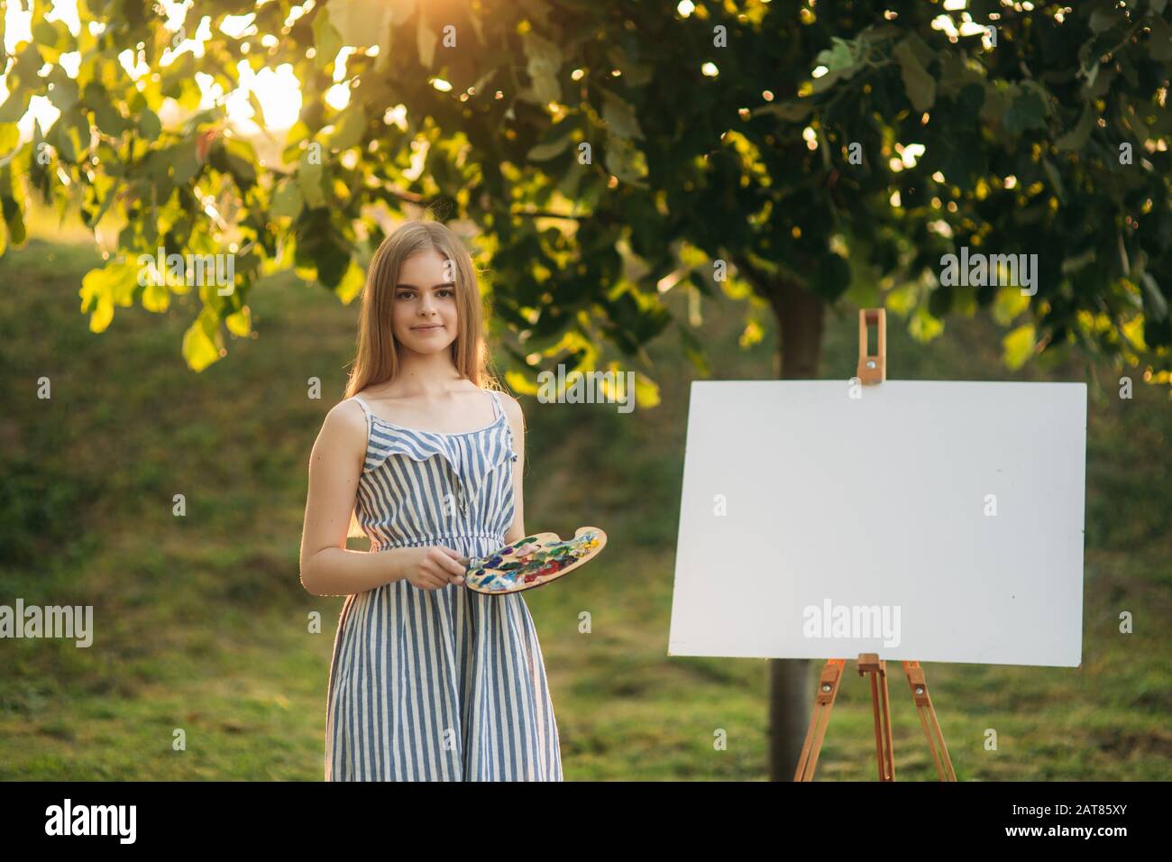 Beautiful girl draws a picture in the park using a palette with paints ...