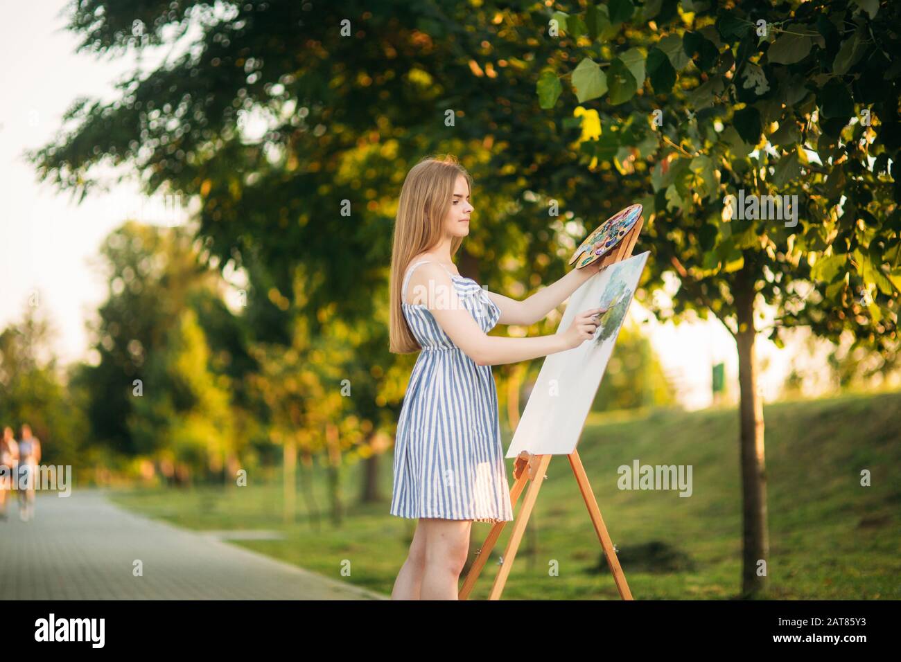 Beautiful girl draws a picture in the park using a palette with paints ...
