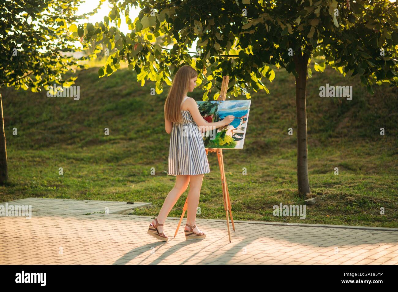 Beautiful girl draws a picture in the park using a palette with paints ...