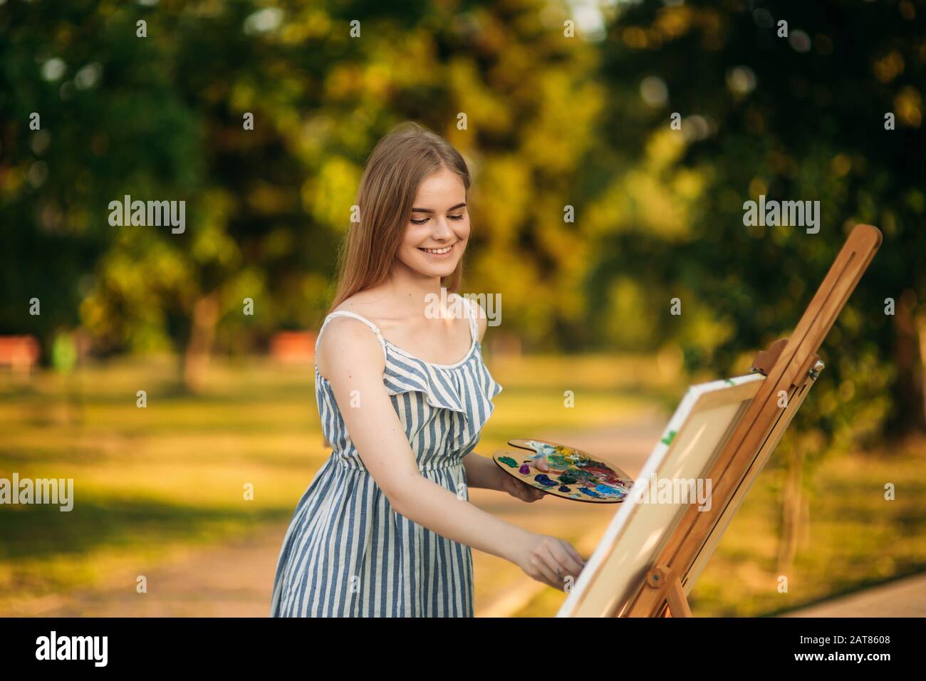 Beautiful girl draws a picture in the park using a palette with paints ...