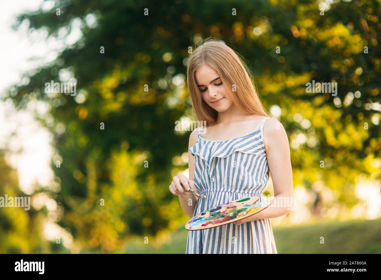 Beautiful girl draws a picture in the park using a palette with paints ...